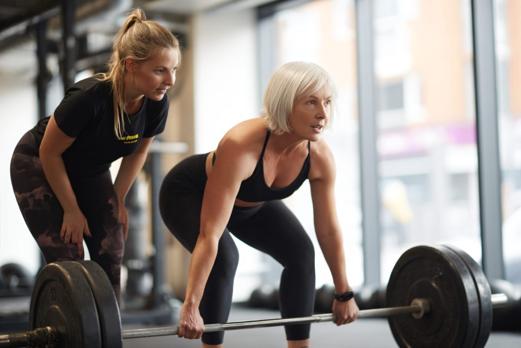 Mujer entrenando peso muerto con su entrenadora personal en el gimnasio