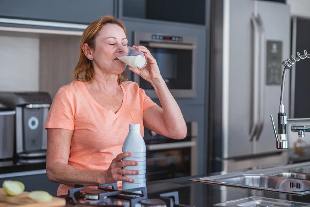 Suplementos después de los 40: mujer bebiendo un batido de proteína en su cocina